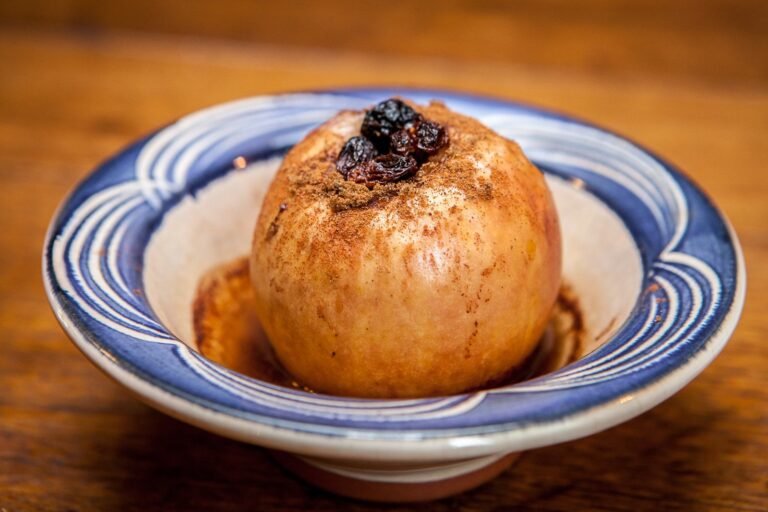 A warm baked apple topped with raisins and cinnamon sugar, served in a blue-and-white patterned bowl.