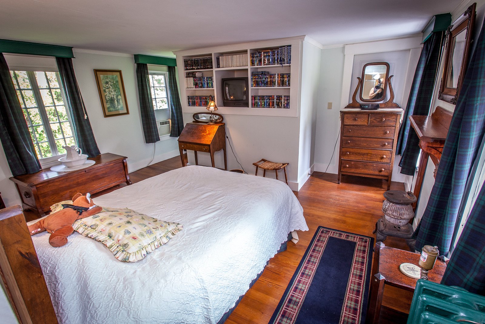 The Blackwatch Room's carved headboard with a dark navy-and-green plaid fabric insert, matching curtains, and a white quilted coverlet.