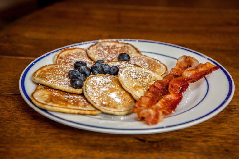 A stack of blueberry pancakes dusted with powdered sugar and served with crispy bacon.