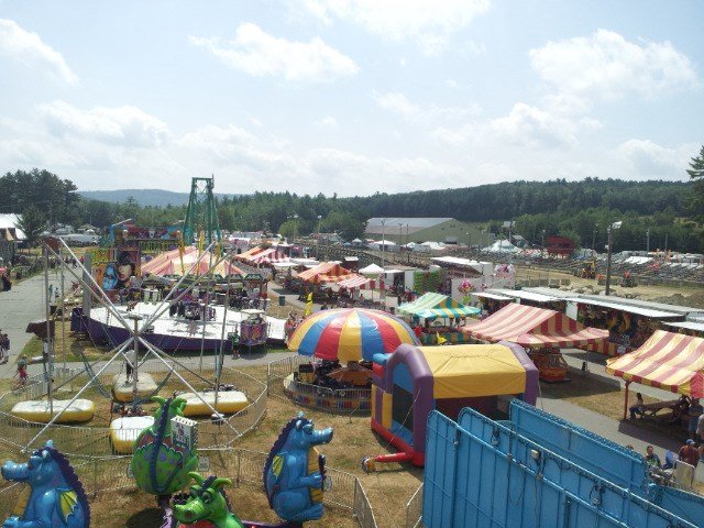 Aerial view of the Cheshire Fair midway in Swanzey, NH, with carnival rides, game booths, and striped tents.