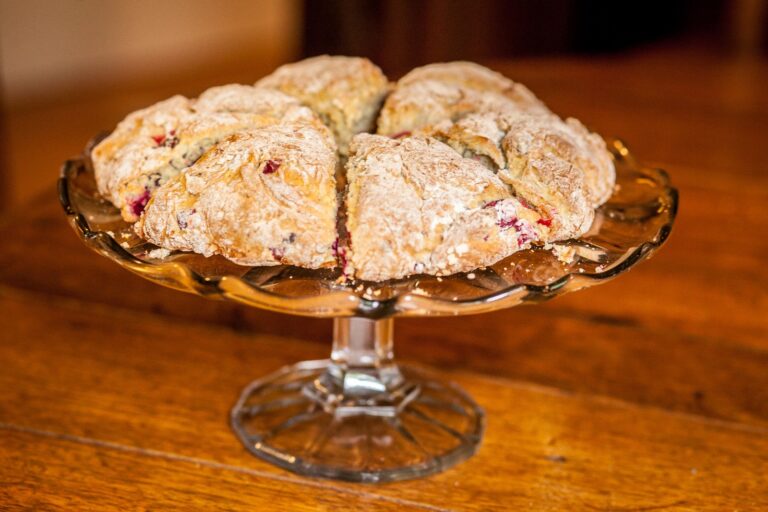 Cranberry scone wedges dusted with powdered sugar on a glass pedestal stand, another angle.