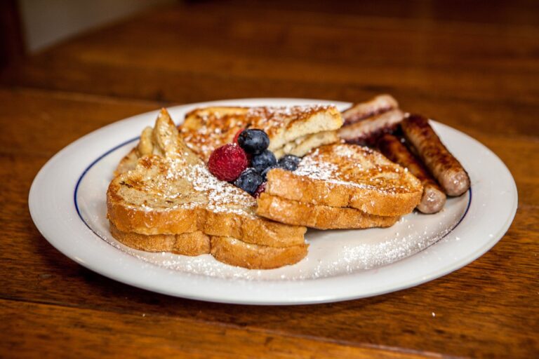 Powdered-sugar-dusted French toast with fresh raspberries and blueberries, served with grilled breakfast sausage.