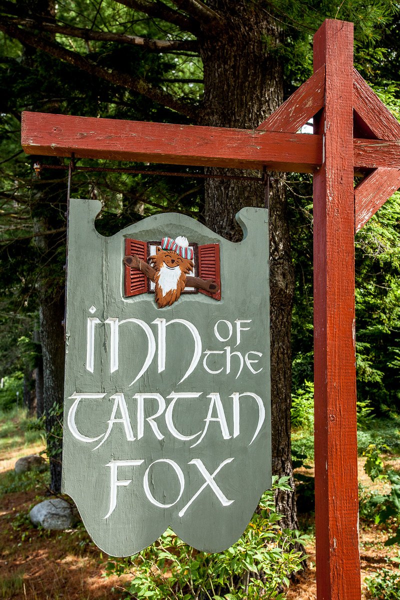The carved fox mascot on the inn's sign, wearing a tam o'shanter and peeking from red shutters.