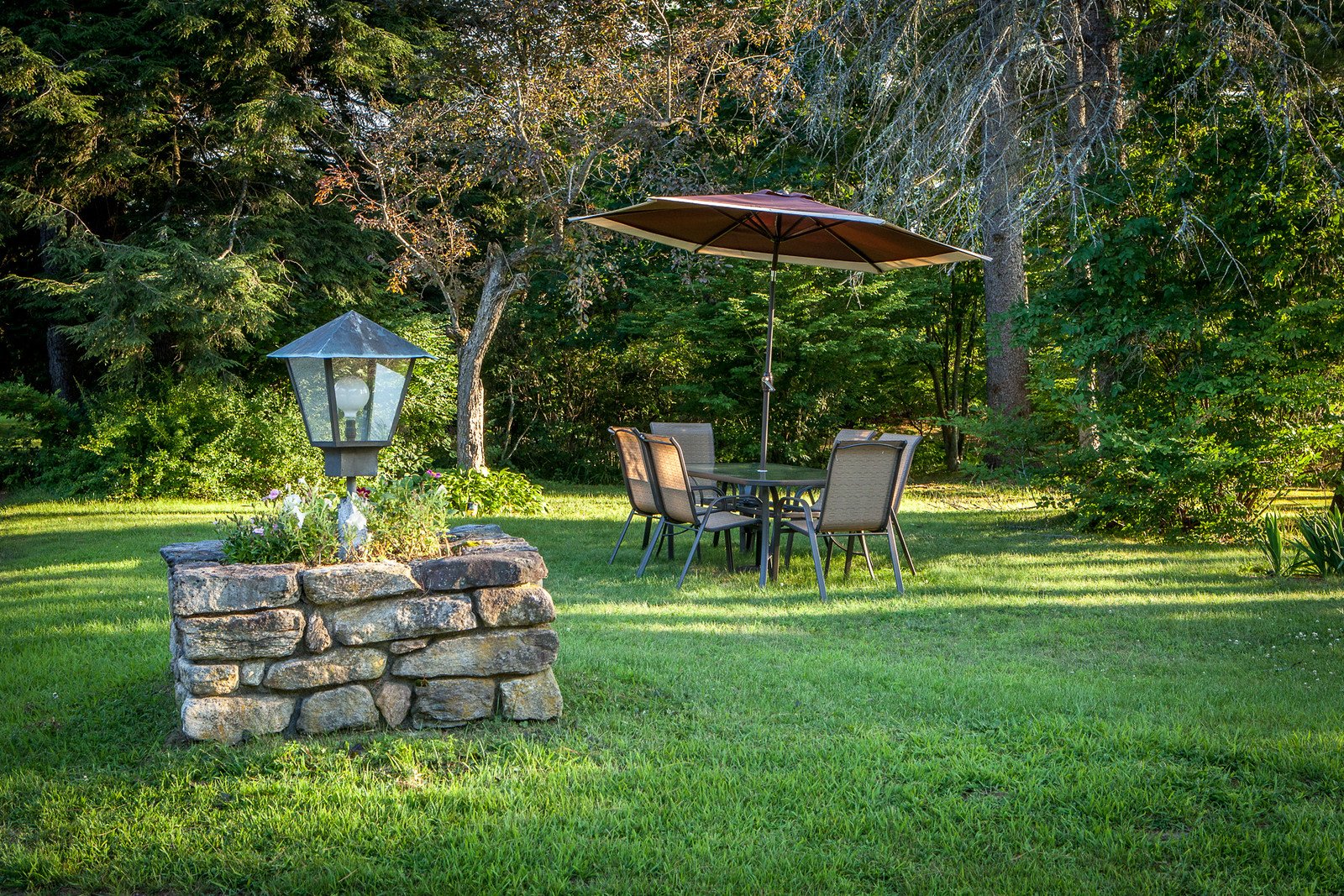 A backyard patio seating area with a round glass-top table, four chairs, and a market umbrella on the lawn.